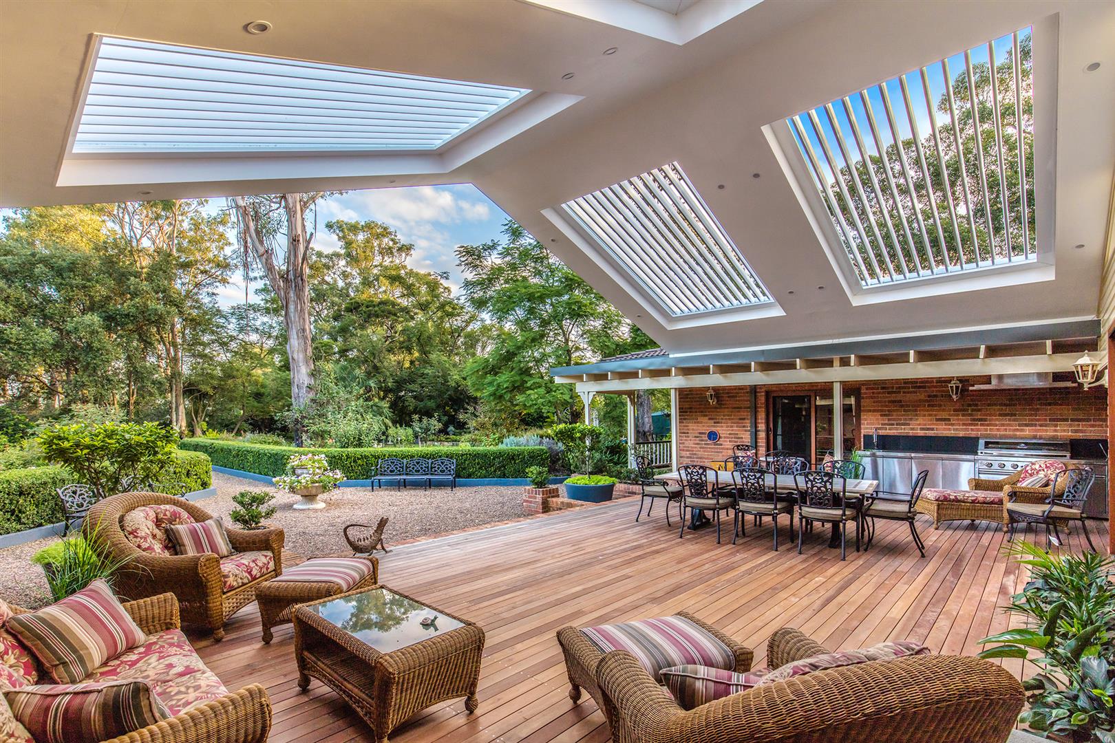 Outdoor entertaining area complete with furniture, outdoor kitchen, and a huge gable roof pergola with opening louvres.